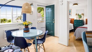 A room with a round table, chairs, a window with a view, a door, and a bed with a headboard. - Seascape Motel & Cottages (Belfast)