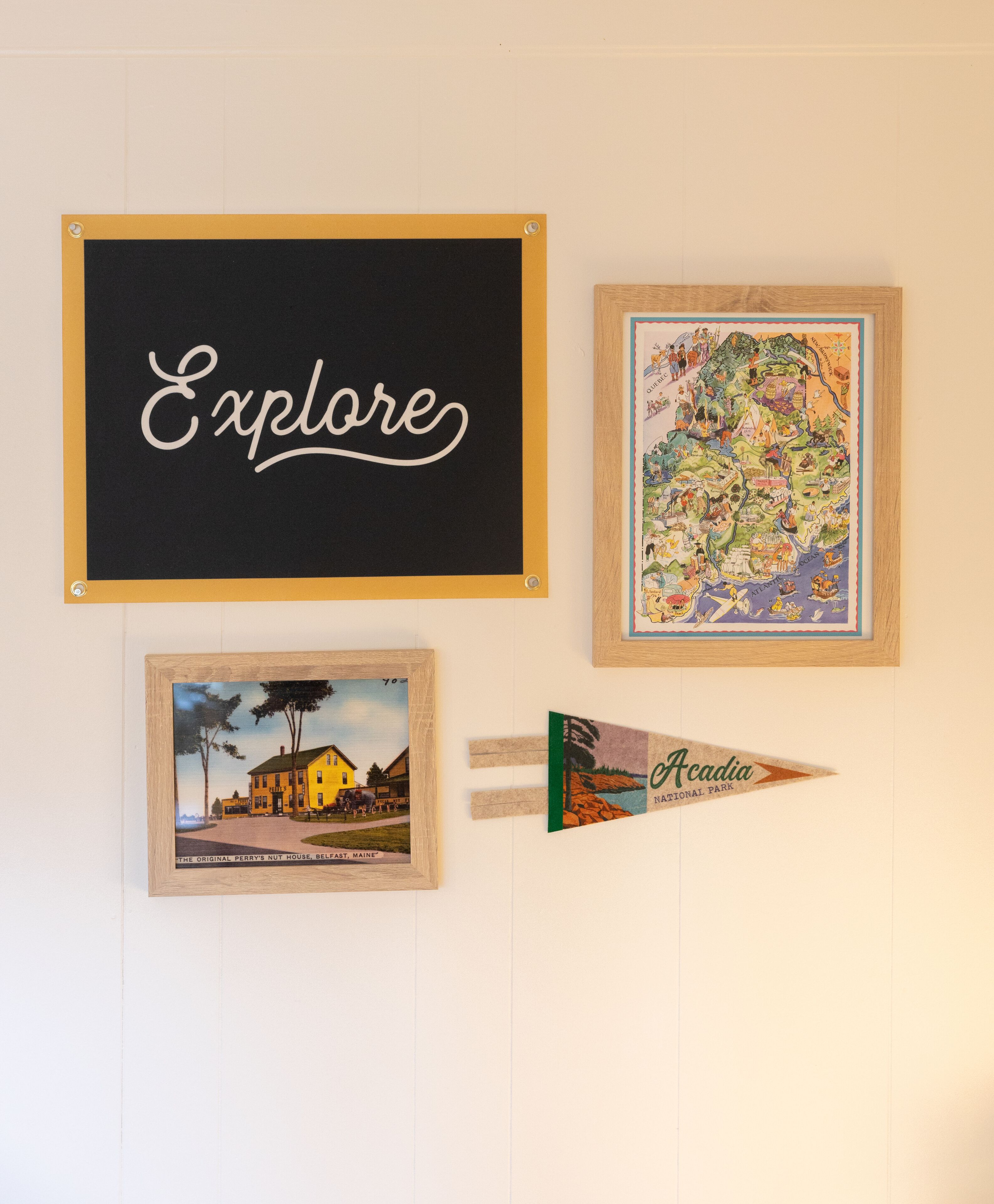 A blackboard with the word "Explore" written on it, a framed map, and a postcard of Acadia National Park.