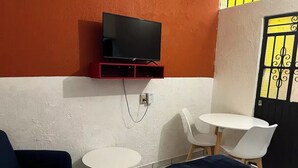 Een hotelkamer met een bed, een aan de muur bevestigde televisie, twee witte ronde tafels en twee blauwe stoelen.