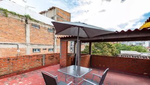 Een dakterras met een metalen tafel en stoelen, een grote parasol en een bakstenen muur.