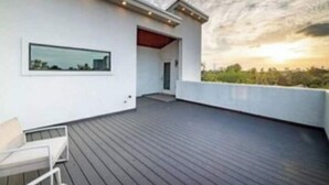 Una terrazza panoramica moderna con pavimento in legno, un'area salotto e vista sul tramonto.