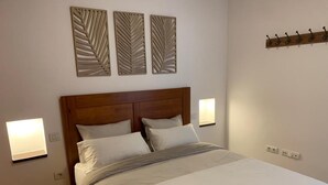 Una cama bien tendida con un cabecero de madera, dos lámparas de noche fijadas a la pared y un motivo decorativo de hojas en la pared.