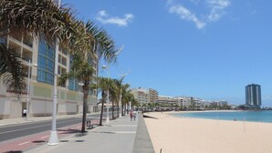 Un paseo marítimo frente a la playa con palmeras, una acera y la arena.