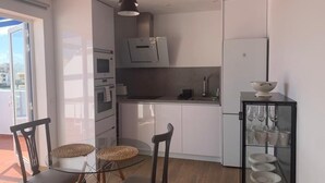 Una cocina moderna con armarios blancos, una mesa de comedor de cristal y una lámpara colgante negra.