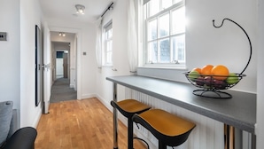 Una cocina moderna con barra, una cesta de frutas y vistas de la ciudad a través de amplias ventanas.