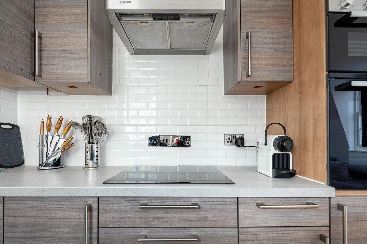 Une cuisine moderne avec des meubles en bois, un dosseret de carrelage blanc et une cuisinière intégrée.