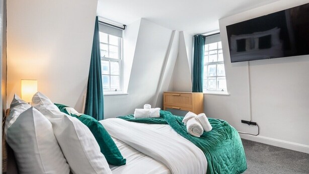 Una habitación de hotel con cama, mesita de noche, televisor y ventana con cortinas.