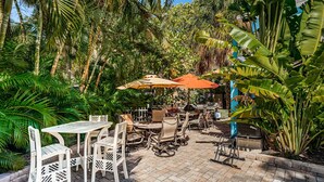 Une terrasse extérieure avec des tables et des chaises, entourée d’une végétation luxuriante et de bananiers.