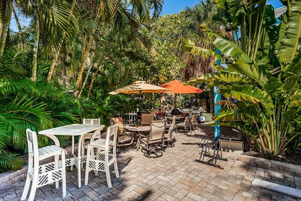 An outdoor patio with tables and chairs, surrounded by lush greenery and banana plants.
