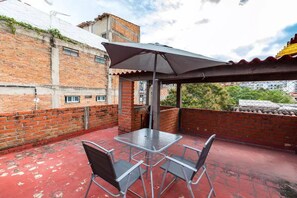 Une terrasse sur le toit avec une table et des chaises en métal, un grand parasol et un mur en briques.