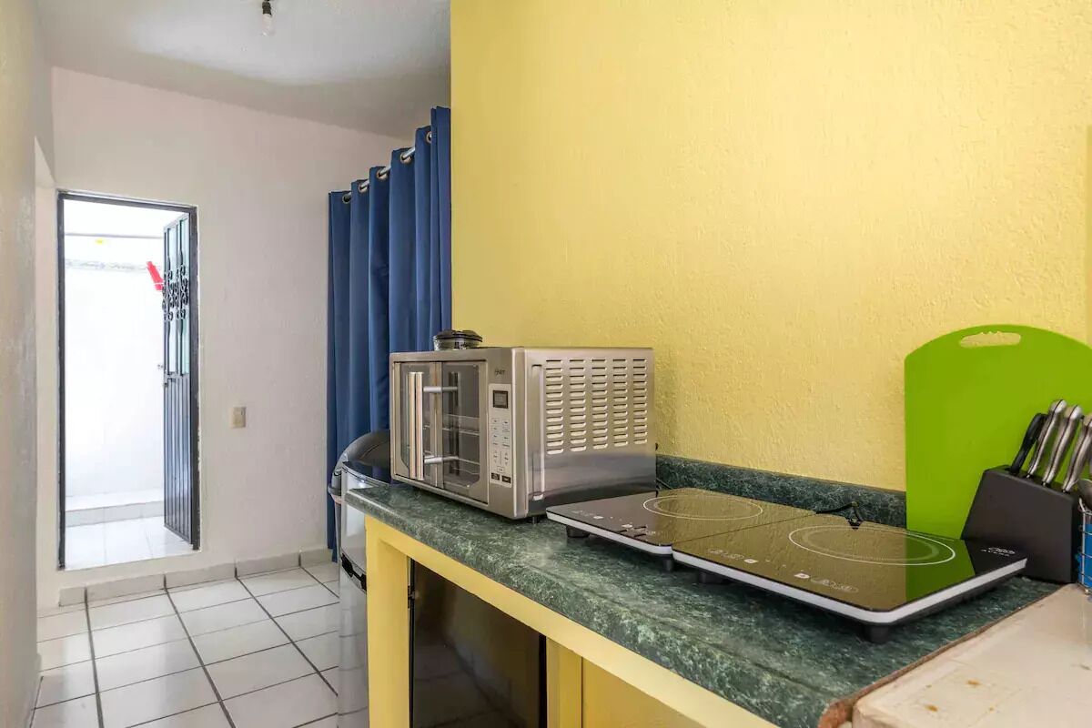 A kitchen with a microwave, toaster, and green cutting board on a countertop.