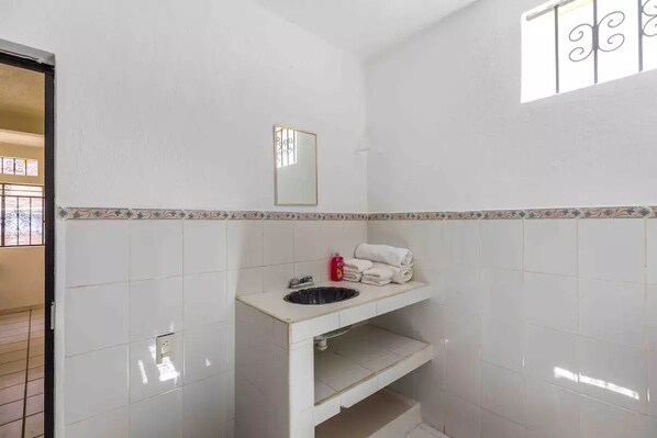 Une petite salle de bain avec des carreaux blancs, un lavabo, un miroir et une fenêtre ornée de barreaux décoratifs.