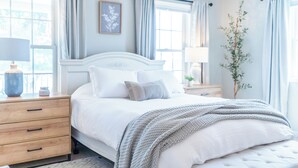 Une chambre à coucher bien rangée, avec un grand lit, des tables de chevet et une fenêtre avec des rideaux.