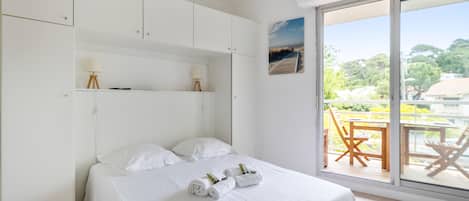 A bedroom with a bed, white walls, a window with a view, and a balcony with chairs.