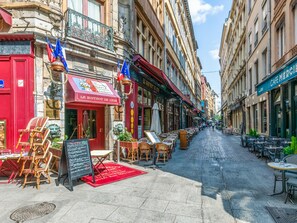A street with outdoor seating, a red awning, and flags.