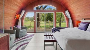Une chambre avec un grand lit, un canapé et un banc. Une porte-fenêtre coulissante donne accès à un espace extérieur d’où l’on peut admirer les arbres et l’herbe.