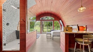 Un intérieur moderne avec un plafond en bois, un lit, un coin repas et une vue sur l’extérieur.
