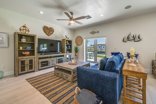 A spacious living room with a large flat-screen TV, wooden entertainment unit, and a blue sofa. - Sebring Serenity: Waterfront Retreat w/ Boat Dock! (Sebring)