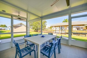 A covered patio with a white table and blue chairs, large windows, and a view of a backyard with a lawn and a house. - Sebring Serenity: Waterfront Retreat w/ Boat Dock! (Sebring)
