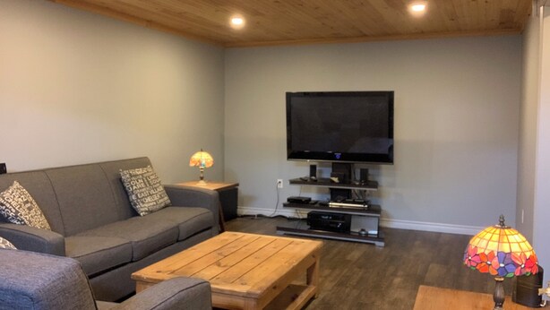A living room with a grey sofa, wooden coffee table, and a flat-screen TV mounted on the wall.