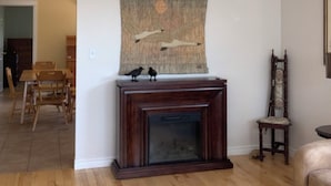 A living room with a fireplace, a painting, and a dining area with chairs and a table.