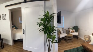 Ein modernes Wohnzimmer mit einer großen Topfpflanze, einer Couch, einem Couchtisch und einem an der Wand montierten Fernseher.