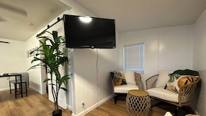 Ein Wohnzimmer mit Flachbildfernseher an der Wand, einem Essbereich mit Tisch und Stühlen und einer großen Kübelpflanze.
