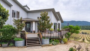 A two-story house with a front porch, steps leading to the entrance, and a view of vineyards in the background. - Be Suite Vineyard Retreat (Paso Robles)