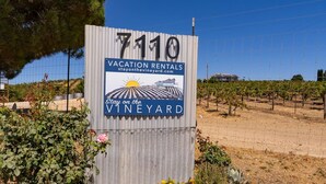 A sign for vacation rentals at 7110, Stay on the Vineyard, with a vineyard backdrop. - Be Suite Vineyard Retreat (Paso Robles)