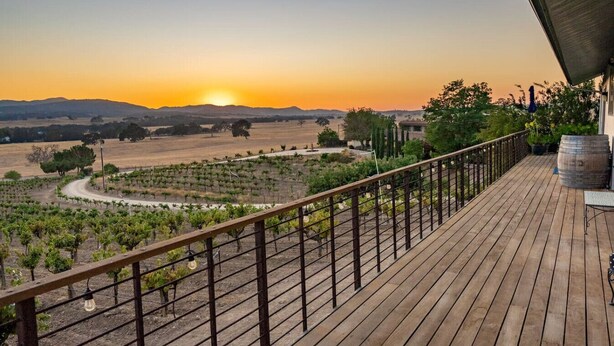 A wooden deck with a metal railing overlooking a vineyard at sunset. - Be Suite Vineyard Retreat (Paso Robles)
