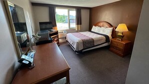 Habitación de hotel con cama, mesita de noche, lámpara, escritorio con teléfono y televisor.