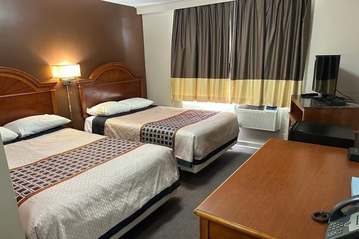 A hotel room with two beds, a desk, a telephone, an air conditioner, and a television.