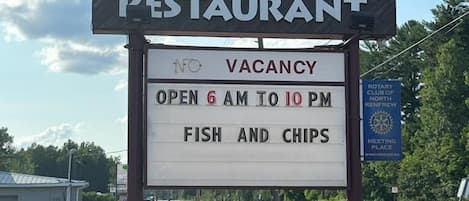 A sign for Bear's Den Lounge & Motel & Restaurant with a vacancy notice, open from 6 AM to 10 PM, offering fish and chips.