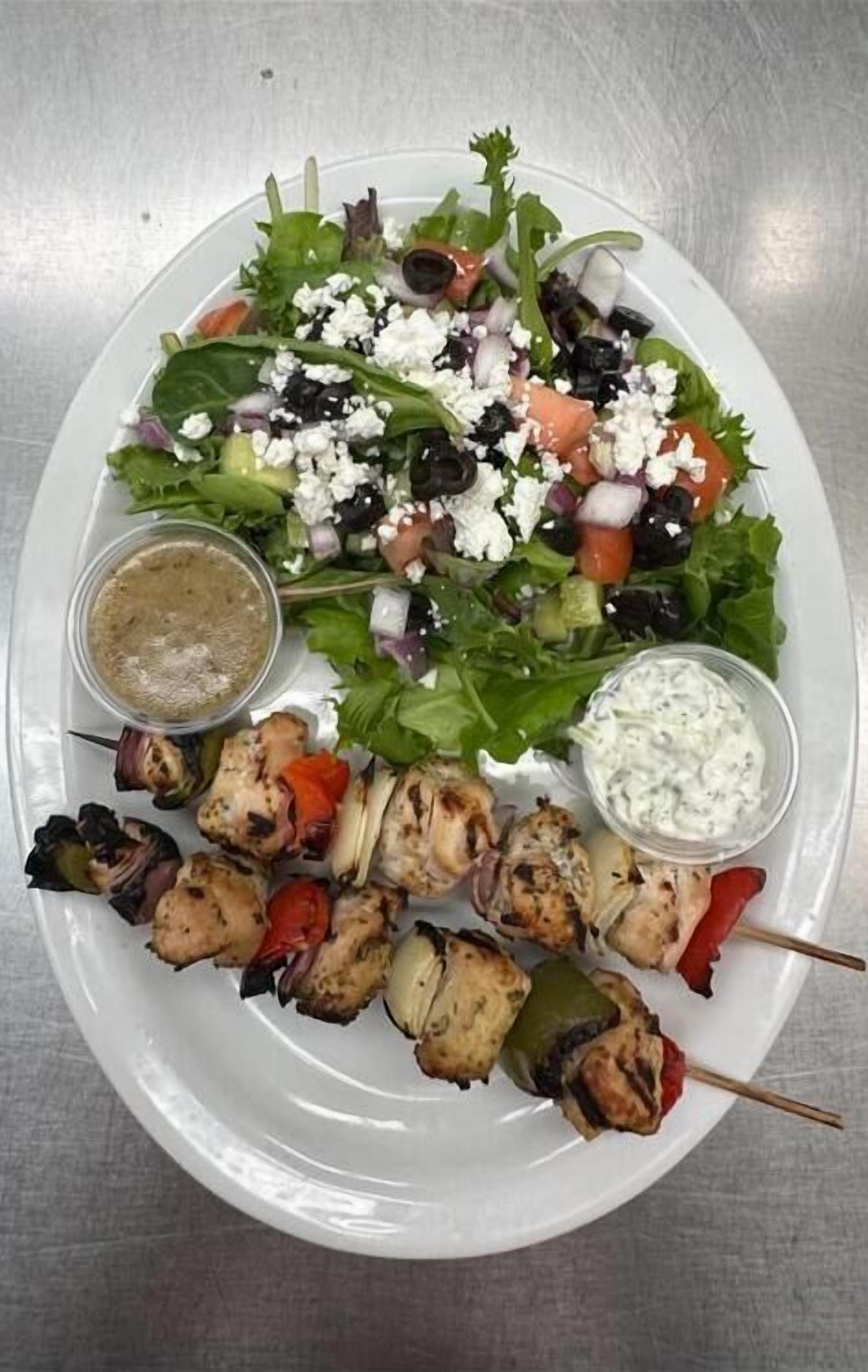 A plate of food including a salad, grilled chicken skewers, and two dipping sauces.