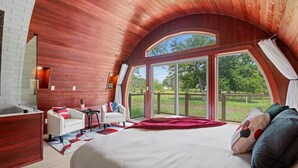 Ein Schlafzimmer mit einem großen Bett, einer Sitzecke mit Sessel und kleinem Tisch und einem großen Fenster mit Blick ins Freie.