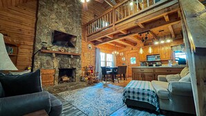 Ein gemütliches Blockhaus-Interieur mit Kamin aus Naturstein, Holzmöbeln, einer Küchenzeile und einem Balkon.