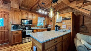 Eine Küchenzeile im Chalet-Stil mit Granit-Arbeitsplatten, Edelstahlgeräten und einer Hängeleuchte.