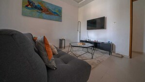 A modern living room with a grey sofa, a coffee table, a painting on the wall, and a flat-screen TV mounted above a black console.