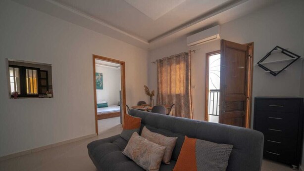 A living room with a grey sofa, a small table, and a cabinet. There is a door leading to another room.