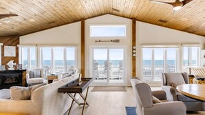 A spacious living area with a high ceiling, large windows offering ocean views, and a cozy seating arrangement. - Oceanfront, Hot Tub, Game Room (Kitty Hawk)