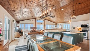 A spacious kitchen with a central island, wooden ceiling, and large windows offering views of the ocean. - Oceanfront, Hot Tub, Game Room (Kitty Hawk)