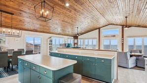A spacious kitchen with a large island, wooden ceiling, and large windows offering ocean views. - Oceanfront, Hot Tub, Game Room (Kitty Hawk)