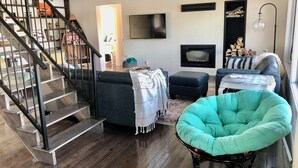Een woonkamer met een trap, een open haard, een televisie en een teal fauteuil.