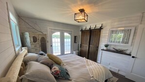 Een slaapkamer met een groot bed, een dressoir, een kroonluchter en een raam met gordijnen.