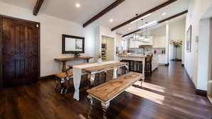 Una cocina amplia con piso de madera, una zona de comedor con un banco, y una puerta grande de madera.