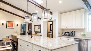 Una cocina moderna con encimera de granito, armarios blancos e iluminación colgante.