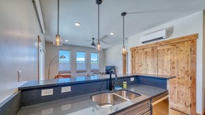 A modern kitchen with a large island, stainless steel sink, and pendant lighting.