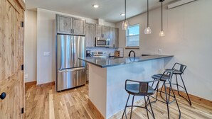 A modern kitchen with stainless steel appliances, a central island with bar stools, and wooden flooring.