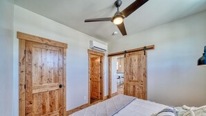A bedroom with a bed, wooden doors, a ceiling fan, and an air conditioning unit.