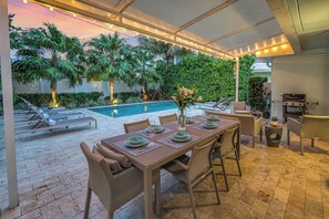 Un espace extérieur aménagé pour les repas, avec une piscine, des palmiers et une terrasse couverte.